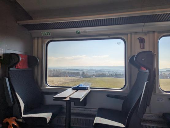 Campagne tchèque ensoleillée prise depuis l'intérieur du train dont les sièges cadrent la fenêtre et sa vue.
