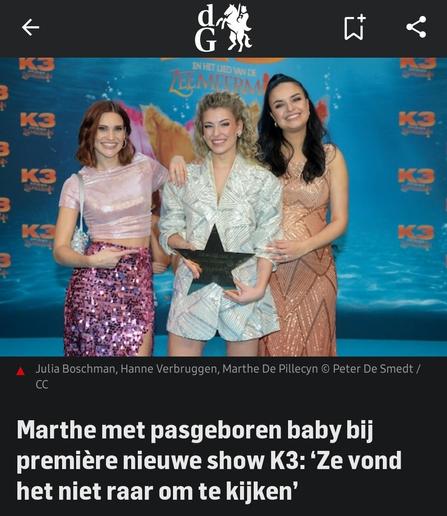 Drie personen van de muziekgroep K3 poseren lachend op de rode loper van de première van hun nieuwe show K3 en het Lied van de Zeemeermin. Ze staan voor een blauwe achtergrond met het K3-logo en een afbeelding van een zeemeermin. De persoon in het midden houdt een stervormige trofee vast. De personen dragen feestelijke outfits: de persoon links heeft een roze glinsterende rok en een crop top, de persoon in het midden draagt een lichtgekleurde jas met een patroon, en de persoon rechts heeft een lange perzikkleurige jurk aan. Alle drie kijken ze blij naar de camera.

Uitgeschreven tekst in de afbeelding:
Logo bovenaan: "dG" met een paard en een ruiter.

Titel van de show op de achtergrond: K3 en het Lied van de Zeemeermin.

Fotocredit onder de afbeelding: "Julia Boschman, Hanne Verbruggen, Marthe De Pillecyn © Peter De Smedt / CC".

Hoofdtekst: "Marthe met pasgeboren baby bij première nieuwe show K3: ‘Ze vond het niet raar om te kijken’".