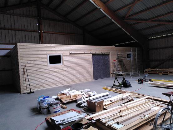 Wooden structure in a wooden hall. The exterior has a wooden slat effect with the dark grey vapour barrier being visible between the exterior planks.