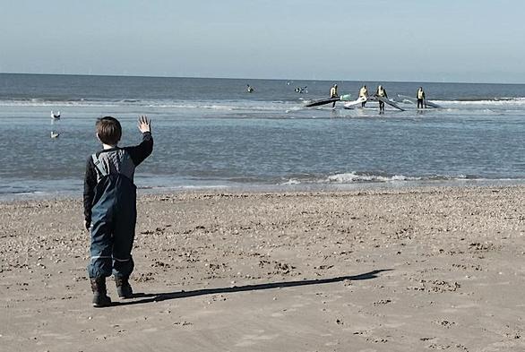 Boy waving at surfski paddlers arriving from the sea.