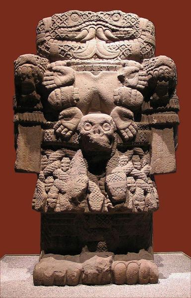 a statue of a rectangular-shaped fearsome serpent-faced deity, hands and skull designs on it, a skull on her stomach, sharp teeth in her mouth, looking at the viewer 