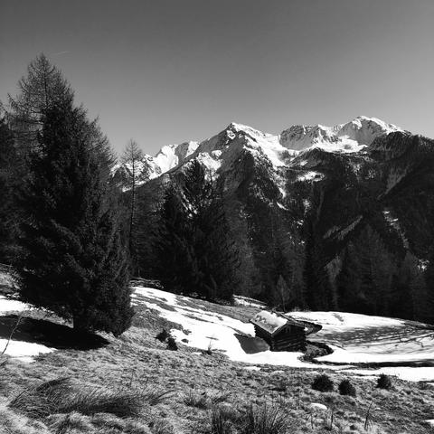 Un prato sottostante con una piccola baracca e le cime innevate delle montagne sulla parte opposta della valle