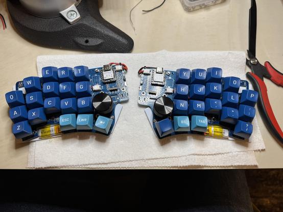 Both halves of Klein split keyboard on the table with some tools. The LiPO batteries have been (jankily) installed at this point.