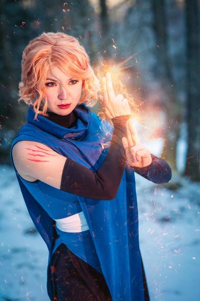 Photo picturing a cosplay  of sypha from Castlevania, made and worn by Keyuricosplay
The character is casting her power of flames with her hands, she is standing in an snowy forest in a powerfull pose