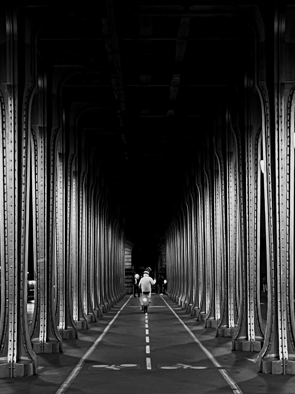 Ein gerader Weg mit Markierungen, auf dem ein Moped davon fährt. Rechts und links ist dieser gesäumt von unzähligen Stahlstützen, auf denen Nieten zu sehen sind.