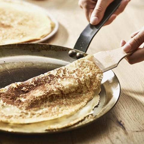 Foto af pandekage, der løftes fra en crepepande med en palet af træ.