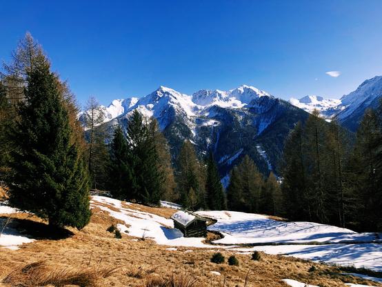 A tiny mountain hut below and the mountain peaks covered by snow in the distance