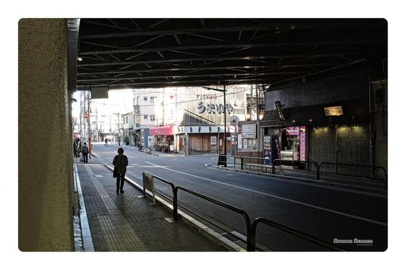 a photograph taken under a train overpass in Asakusa.  The tunnel is dark but the city outside is bright and warm.  The photograph is tinted to look like film, with the colors and contrast artistically tinted. 