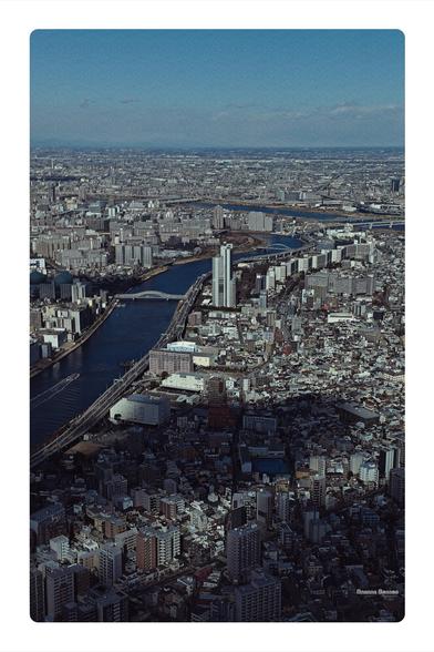A photograph taken from high up on the Tokyo Skytree overlooking some of the Sumida river and a large chunk of Tokyo.  The photograph is tinted and a little noise applied to look like film.