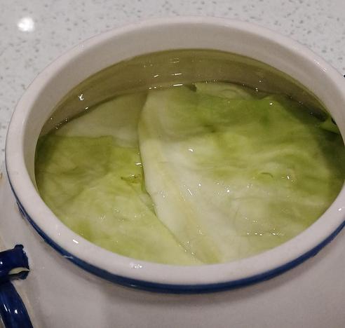 The shredded cabbage is stuffed in a big ceramic jar with leaves over top, and the salty liquid is just covering the whole assembly.