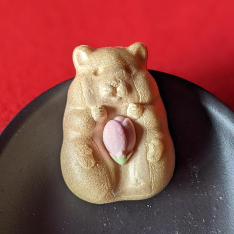 A hamster monaka (wafer) holding a sugar cherry blossom bud.