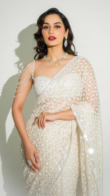Manushi Chhillar's latest appearance in a white Manish Malhotra saree is a testament to timeless fashion. The organza saree's geometric and floral patterns shimmer gracefully, while the modern bralette blouse with a sweetheart neckline enhances her silhouette. With bold red lips and soft vintage-inspired curls styled by David, Manushi embodies elegance and charm.