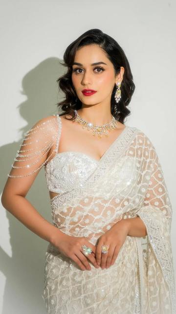 Manushi Chhillar's appearance in a white Manish Malhotra saree redefines elegance. The luxurious organza fabric, adorned with intricate geometric and floral embroidery, flows gracefully. The cropped bralette blouse with a sweetheart neckline and cascading beadwork adds a modern touch. Complemented by a Dintara Jewels choker and bold red lips, Manushi's ensemble is a fashion masterpiece.