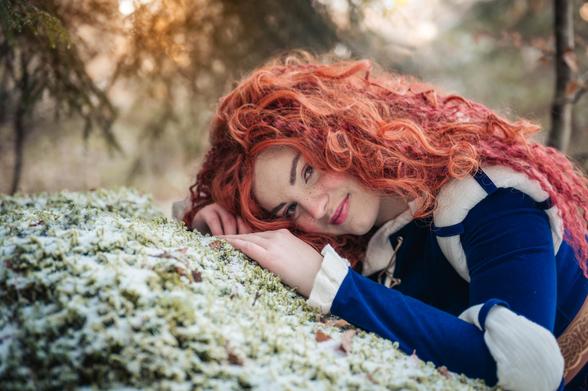 cosplay photo of Merida from tangled
Merida is resting in a snowy forest smiling at the camera
The mood of the photo is soft with a warming light in the back