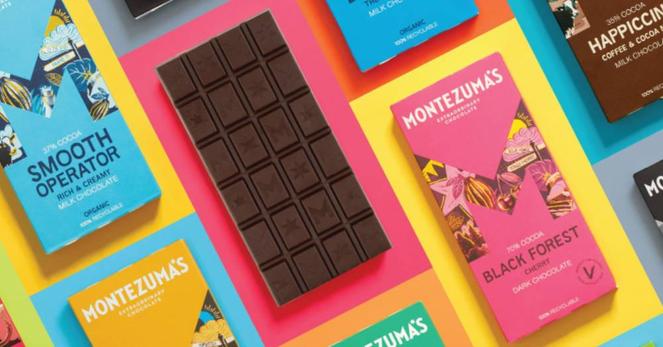 Eine bunte Collage in deren Mitte eine dunkle unverpackte Tafel Schokolade liegt. Daneben in hellen bunten Farben verpackte Schokoladen (Pink, Hellblau, Gelb). Darauf ist der Markenname "Montezuma's" zu erkennen.