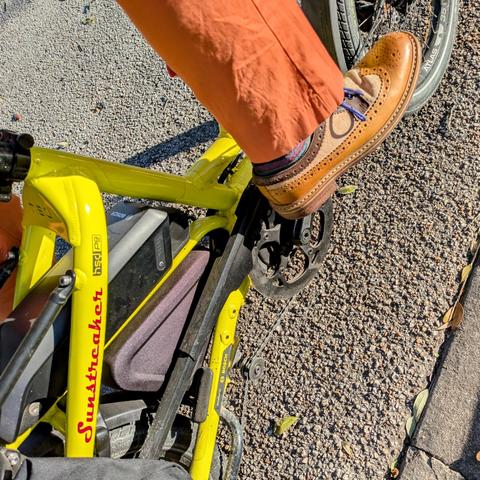 A photo of my right foot on the pedal of a 

yellow Tern HSD cargo bike with its name, Sunstreaker, in red on the seat stay

I'm wearing

tan leather & beige canvas wingtip spectator derby with purple laces under an orange pantleg