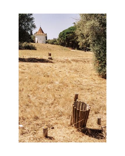 public park with an wooden trashcan in the foreground, a yellow dried out meadow and in the background a tiny white round house