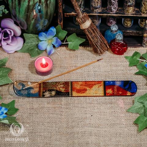 An example of the Sabbats Glass Incense Holder is sitting on a burlap-covered surface. It is transparent glass printed with colorful translucent panels containing symbols for each of the 8 pagan sabbats. Presented by Inked Goddess Creations.
