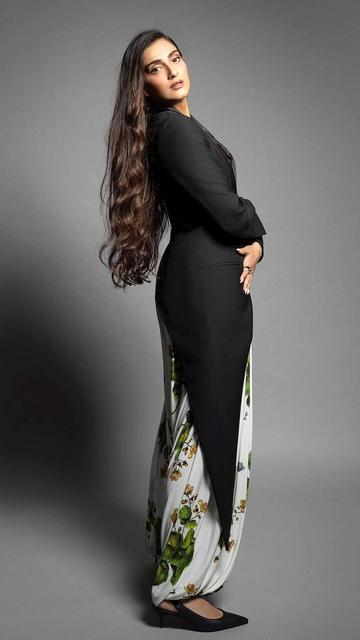 In a stunning display of fashion innovation, Sonam Kapoor combines a tailor-fit black blazer with draped harem-style pants adorned with large green leaves and yellow flowers. The high-waisted, billowy silhouette of the pants contrasts beautifully with the blazer's structured design. Accessorized with a Loewe handbag and Louboutin heels, Sonam's look is a perfect blend of sophistication and flair.