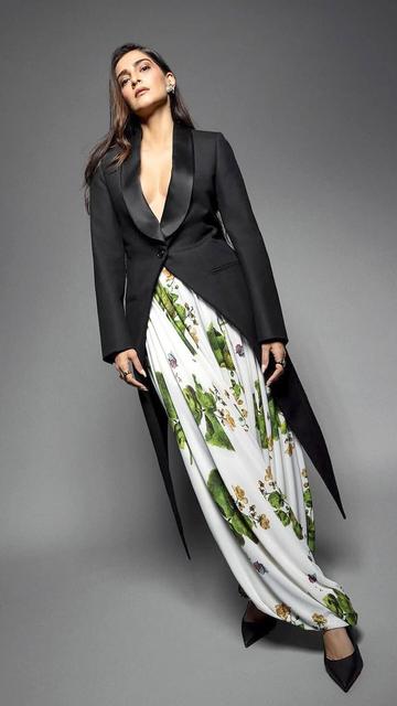 In her recent appearance, Sonam Kapoor dons a black blazer with a plunging neckline alongside draped harem-style pants featuring vibrant floral patterns. The fusion of formal and bohemian styles is accessorized with a sleek Loewe handbag and classic Louboutin heels. Her natural makeup and voluminous waves complete the look, highlighting her fashion-forward approach.