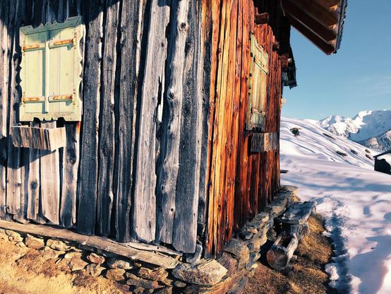 A wooden cabin with different tones on the wood and mountain peaks in the distance