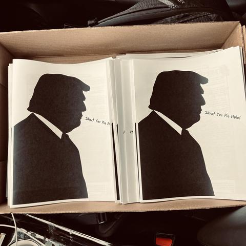 a box filled with copies of a printed magazine with the shadow of Donald Trump on the cover, saying "Shut yer Pie Hole!"
