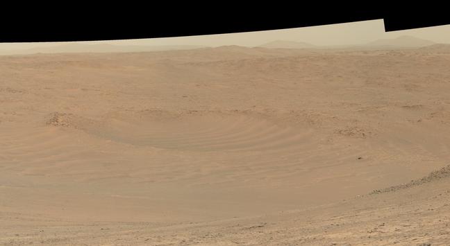 An ochre toned picture of a Martian landscape featuring a large crater filled with dunes.