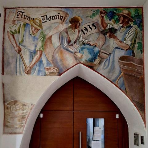 Fresco of working farmers above a point arch door.