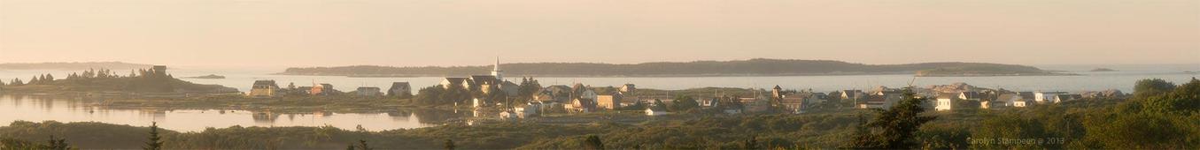 A very long vertical image.  We are on a hill looking down on a picturesque village along the ocean.  The lighting is coming from the left, behind us, and is bathing the scene in a pink glow.  There is a soft mist. The water is calm, slightly left of middle is a church steeple. We can see islands off the shore and between us and the homes are black oak, wild rose bushes and other green shrubbery. 