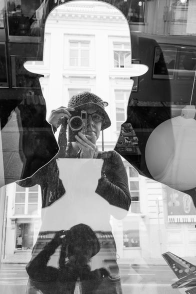 Black and white autoportrait in a mirror in the shape of a male bust with a bowler hat in a shop window in Brussels.