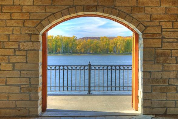 An arched stone doorway frames a scenic view of the Mississippi River band lush trees in the distance.