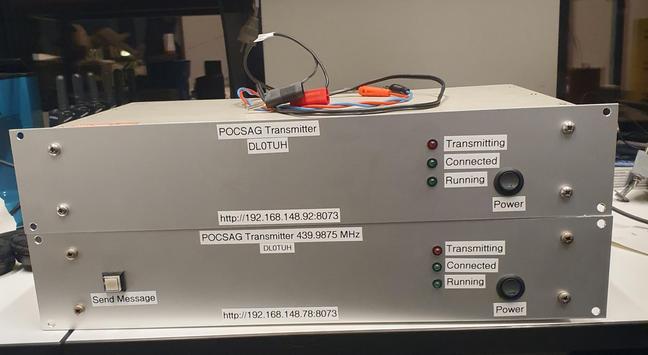 Two almost identical transmitters. They are grey metal boxes which will fit into a rack. Both transmitters have a front plate with labelled powerbutton snd status LEDs for transmitting, connected, and running. The original first transmitter at the bottom has an additional "send message" button.