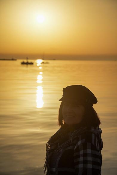 Sonnenuntergang am Hafen von Triest, im Hintergrund das Meer im Licht der untergehenden Sonne. Im Vordergrund eine Dame mit Käppi und Schal. Die Dame ist fast nur als Silhouette erkennbar
