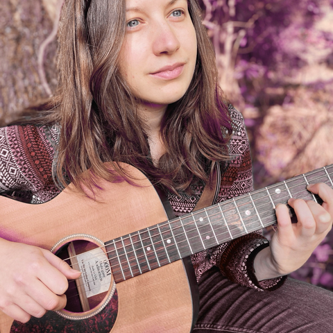 Photo de Lena Redwood avec sa guitare folk dans un bois.