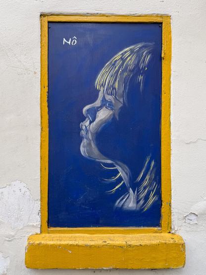 The photo shows a drawing of a child's face in profile, in blue hue. The yellow frame represents the edge of an old window. The photo was taken outside.