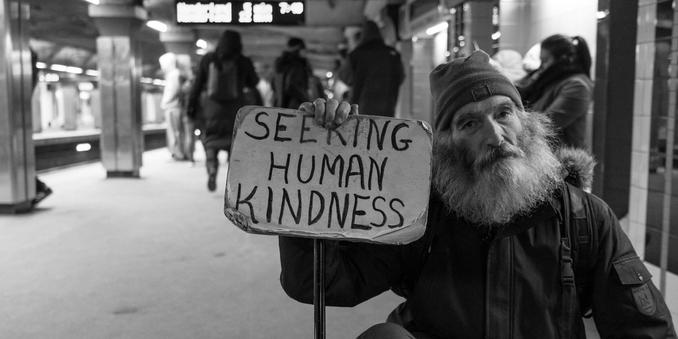 Homeless man holding that reads 'seeking human kindness.'