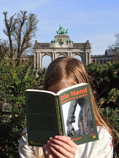 Ein Mädchen steht vor dem Triumphbogen in Brüssel und liest in dem Buch "Die Hand".