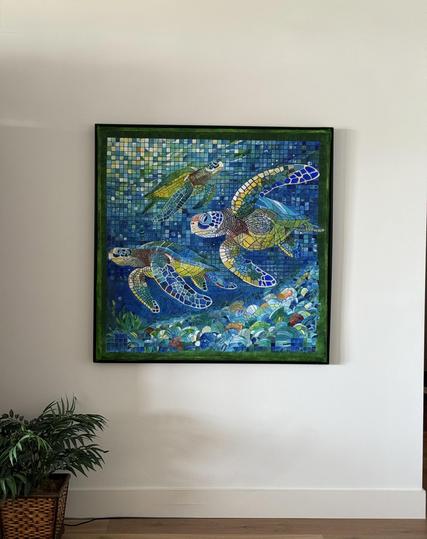Three sea turtles, painted in pointillism. Sea greens and blue cover the work as sunlight lands on the surface, brightening the entire picture. The work, done in a mosaic style, took over 6 months to complete. It is 46X46" and is on a white wall with black frame.