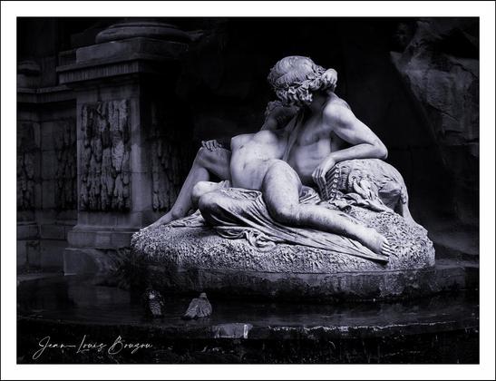 The image showcases a beautifully carved marble sculpture of Acis and Galatea, set against a dark backdrop that amplifies its intricate details. At the center, two figures embrace in an intimate pose, their bodies skillfully rendered to evoke a sense of movement and tenderness. The texture of the marble highlights the play of light and shadow, enhancing the emotional connection between the figures.
The fountain setting adds a serene ambiance, suggesting a moment frozen in time. Water trickles gently around the sculpture, emphasizing a theme of life and continuity. The surrounding architecture, though faint, hints at grandeur and history, lending a timeless quality to the scene.
Interpretively, this sculpture could symbolize love, desire, or the beauty of human connection. The contrast between the softness of the figures and the hardness of the marble might also speak to the enduring nature of love amid the transient aspects of life. Overall, the image invites viewers to reflect on the nuances of passion and permanence.