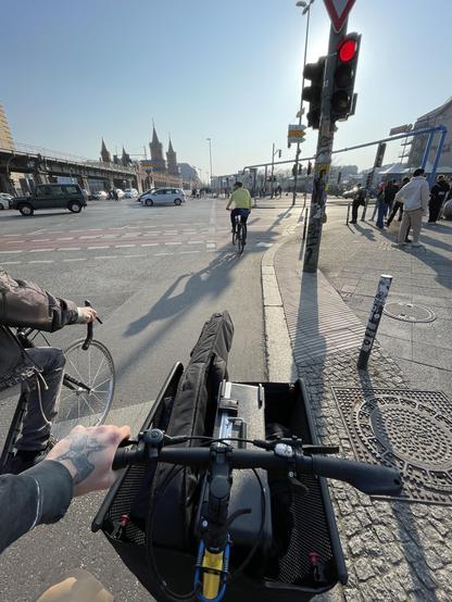 Photo of a yellow cargo bike packed with some music equipment, standing at a red traffic light, looking towards the Oberbaumbrücke in Berlin.