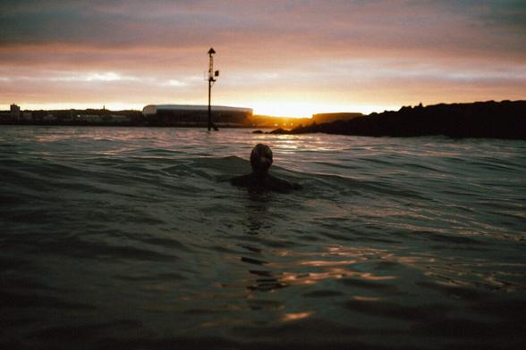 A person swims in the ocean at sunset.