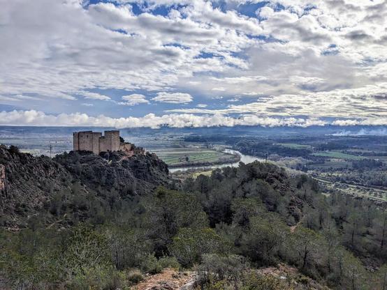 A wide shot of a landscape with the Miravet castle and the Ebre river in the background