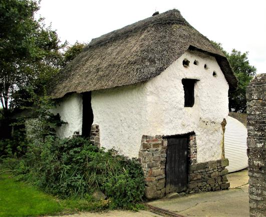 A mostly whitewashed building with stone base and thatched roof. In the end wall are holes for doves to enter.