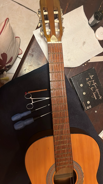 Outils de démontage : une pince, un tournevis, le manche de la guitare, les mécaniques posées consciencieusement dans l’ordre. 