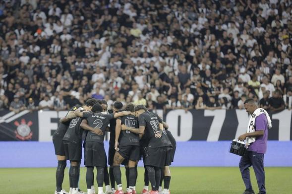 Foto dos jogadores do Corinthians em roda. A torcida na arquibancada como plano de fundo.