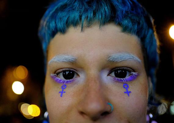 A young woman with blue hair, black eyes, grey eyebrows and purple female symbols painted under here eyes.