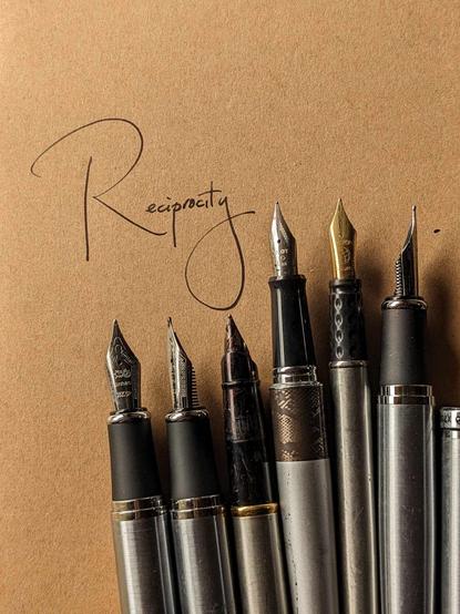 an array of fountain pens with the word Reciprocity written above them in black ink