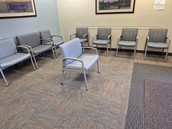 It's a long chair sitting in the middle of a bunch of other chairs in a waiting room.