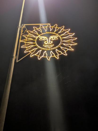 Sur une lanterne de rue est accroché une lumière à la forme d'un soleil et de la tête de St Maurice, emblème de la ville de St Moritz