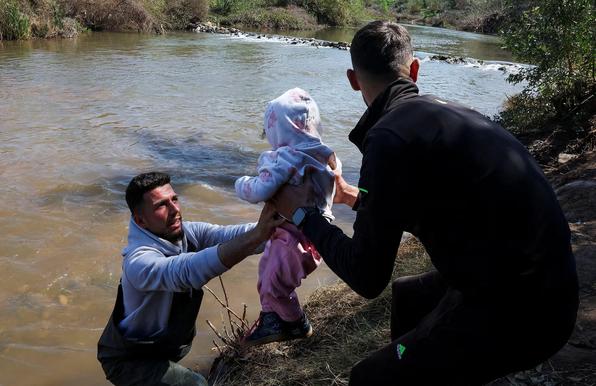 A man is passing a baby to another man, about to cross a river.